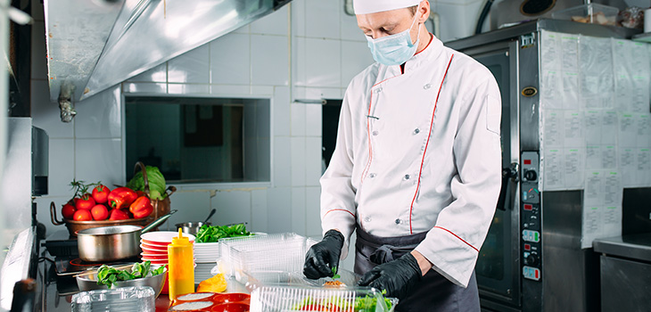 homem com roupas de cozinheiro preparando a comida em embalagem na dark kitchen.