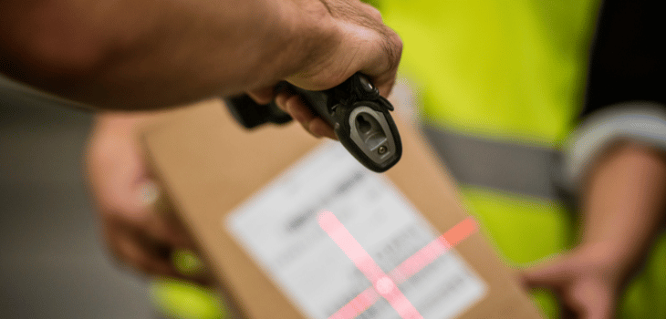 Homem apontando o leitor de código d de arras pra uma caixa, que está sendo segurada por outro funcionário.